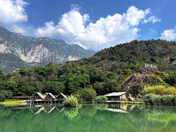 laghetto con palafitte e scritta archeopark sulla montagna